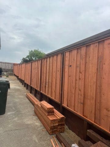 Cedar privacy fence under construction with stacked boards nearby