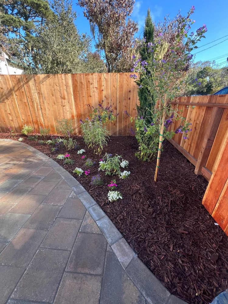 Wood fence corner with a fresh mulch bed and pavers