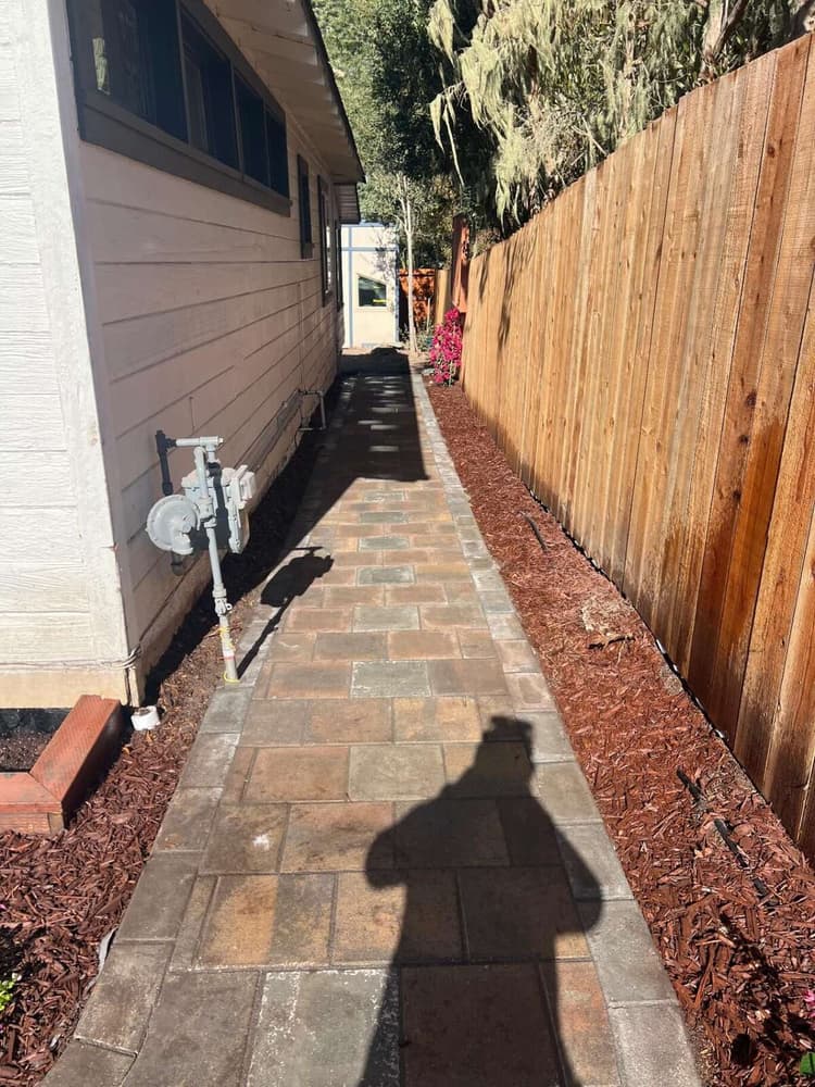 Paver walkway along the side of a house beside a new wood privacy fence